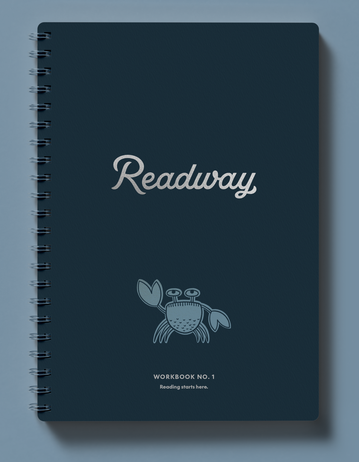 A spiral-bound workbook titled 'Readway' on a dark navy cover, featuring a light blue crab illustration and small text reading 'WORKBOOK NO. 1' and 'Reading starts here.